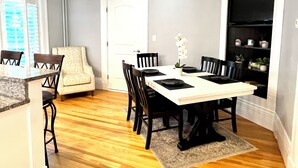 A dining area with a white table, black chairs, and a beige armchair. There is a white door and a shelf with plants. - Stylish home next to train to Boston, near Salem (Wakefield)