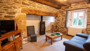 Una habitación rústica con paredes de piedra, chimenea, televisor, una mesa de centro de madera y un sofá.