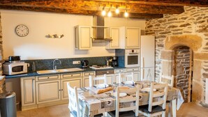 Cocina compacta con armarios blancos, microondas, lavamanos y pared de piedra.