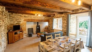Una habitación rústica con paredes de piedra, techo de madera, una mesa de comedor dispuesta para cuatro personas y un televisor sobre un mueble de madera.