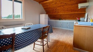 A kitchen with a wooden ceiling, a dining table with a polka dot tablecloth, and a view of trees through the window. - Apartment 4/6 persons (AUMONT-AUBRAC)