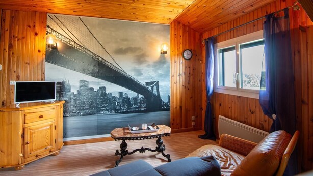 A cozy room with a wooden interior, a large window with curtains, a television on a wooden cabinet, and a table with a tray of snacks. - Apartment 4/6 persons (AUMONT-AUBRAC)