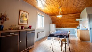 A cozy kitchen with wooden ceiling beams, a dining table with chairs, and a window providing natural light. - Apartment 4/6 persons (AUMONT-AUBRAC)