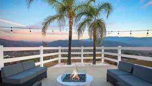 An outdoor seating area with a fire pit, white fence, and a view of distant mountains. - Grenache Estate - Nestled in Temecula Wine Country (Temecula)