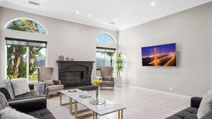 A modern living room with a fireplace, comfortable seating, and a large window offering a view of greenery. - Grenache Estate - Nestled in Temecula Wine Country (Temecula)