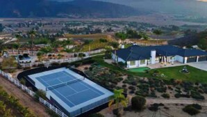 A large building with a tennis court, surrounded by landscaped gardens and hills in the background. - Grenache Estate - Nestled in Temecula Wine Country (Temecula)