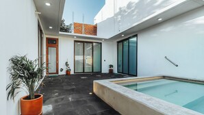 Area piscina moderna all'aperto, con bordo in cemento, piante in vaso e una porta in vetro che dà su un edificio in mattoni.