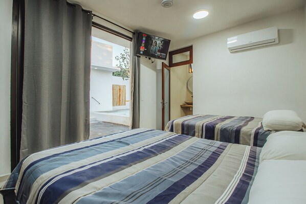A hotel room with two beds, a television, an air conditioning unit, and a view of the outside. - Casa Romira (La Manzanilla)