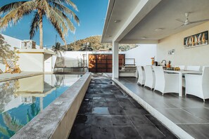 A modern outdoor pool area with a seating area, a palm tree, and a mountain view. - Casa Romira (La Manzanilla)