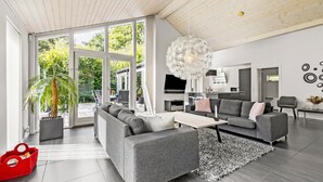 A modern living room with a grey sofa, a coffee table, and a large window overlooking a garden.