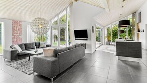 A modern living room with a grey sectional sofa, a coffee table, and a large window offering a view of greenery.