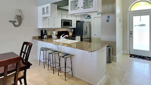 A modern kitchen with white cabinets, a granite countertop, a central island with bar stools, and a microwave. - Banana Bay Townhome #13932 by Southern Vacation Rentals (Pensacola)