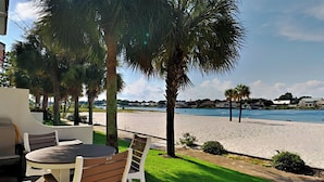 An outdoor patio with a table and chairs, a grassy area, and a view of a beach and water body. - Banana Bay Townhome #13932 by Southern Vacation Rentals (Pensacola)