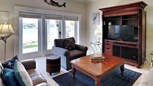 A living room with a ceiling fan, a television on a wooden cabinet, a sofa with cushions, a coffee table, and a view through the glass doors. - Banana Bay Townhome #13932 by Southern Vacation Rentals (Pensacola)