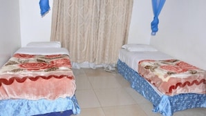 Two single beds with floral bedding, a beige curtain, and blue drapes. - City Side Hotels and Apartments Mukono (Mukono)