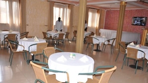 A restaurant with round tables and chairs, a tiled floor, and a television on the wall. - City Side Hotels and Apartments Mukono (Mukono)