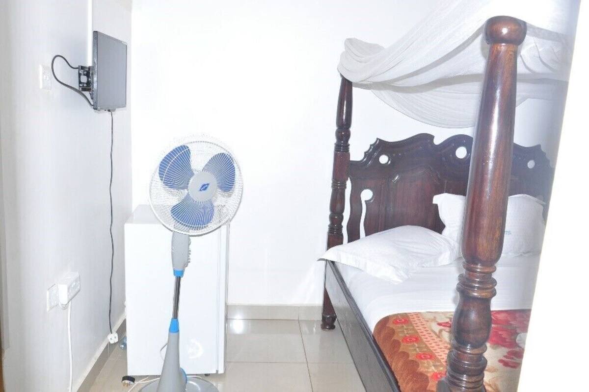 A bedroom with a bed, a standing fan, and a wall-mounted heater.