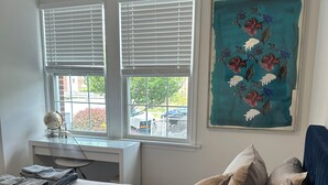 A bedroom with a bed, two windows, a desk, and a painting.
