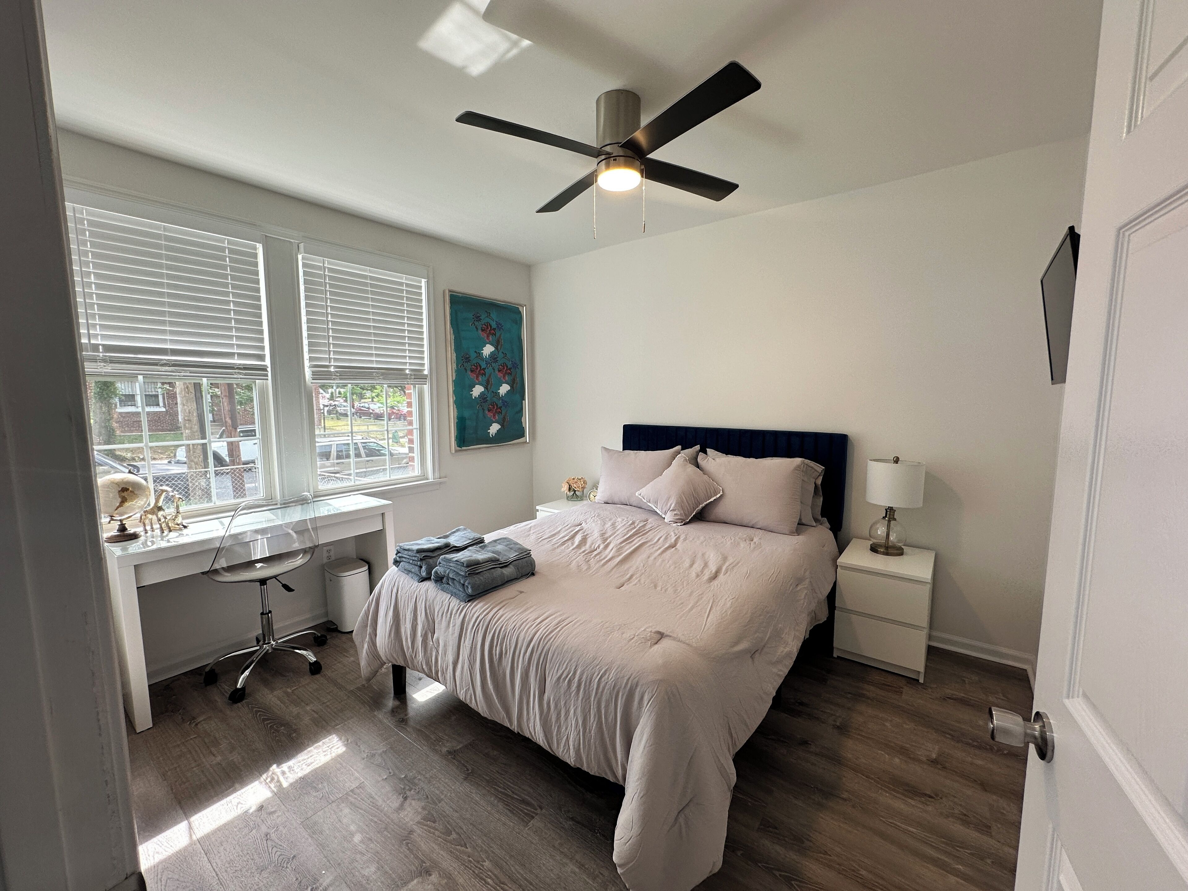 A bedroom with a bed, desk, chair, and a ceiling fan.