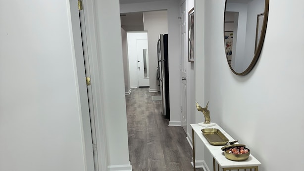 A hallway with a white door, a white console table with a gold mirror, and a gray wooden floor.