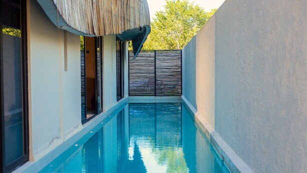 Una piscina estrecha con una estructura de techo de paja encima, rodeada de muros y un portón.