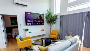 Una sala de estar moderna con una televisión de pantalla plana, un sofá, un sillón amarillo y una planta en maceta.