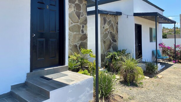 A modern house with a black door, stone wall, and a covered porch with chairs. - Casa Anguiano Valle de Guadalupe (Valle de Guadalupe)