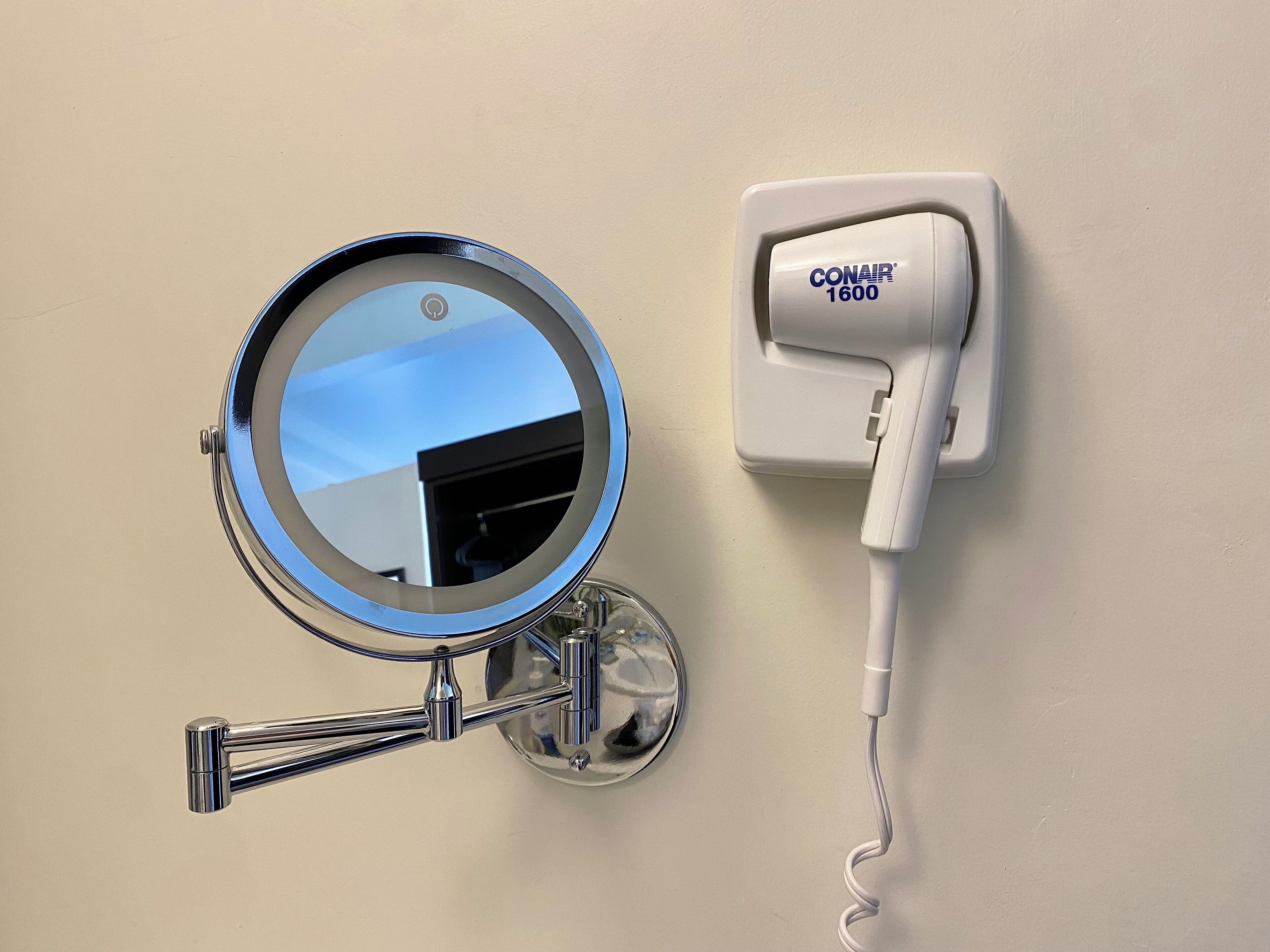 Un espejo montado en la pared con un marco cromado y un adaptador de corriente CONAIR 1600 conectado.