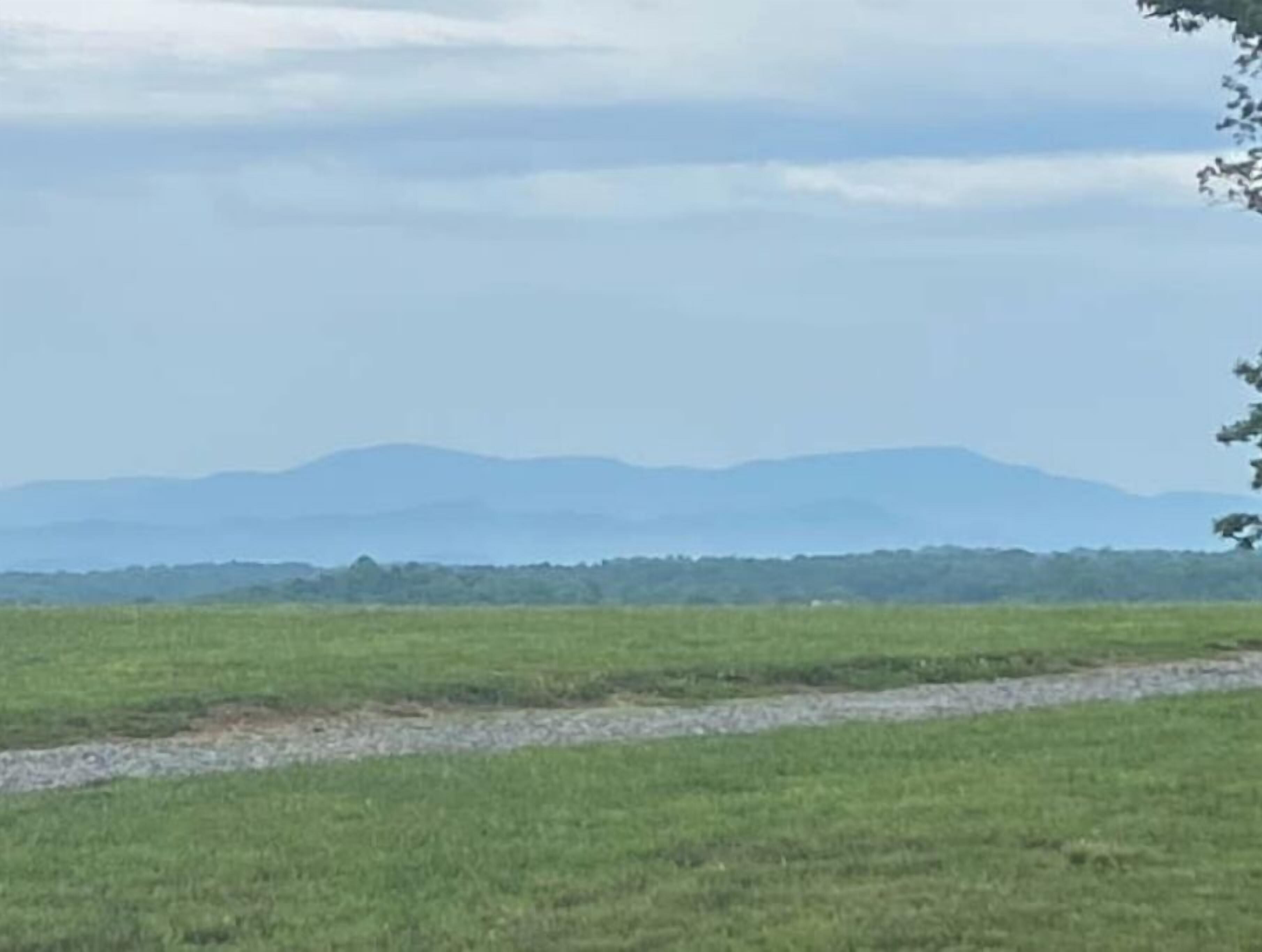 A wide, open field with a distant mountain range under a cloudy sky.