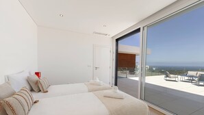A modern bedroom with two beds, a large sliding glass door leading to an outdoor patio with seating. - Poolside and Seaview Villa (Lisboa)