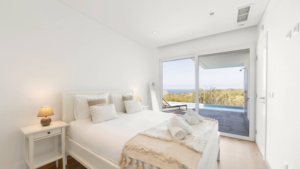 A modern bedroom with a large bed, a nightstand, and a view of the outdoors. - Poolside and Seaview Villa (Lisboa)