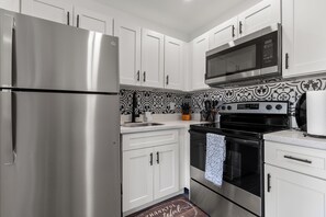 Une cuisine moderne dotée d’appareils électroménagers en acier inoxydable, de meubles blancs et d’un revêtement mural décoratif.