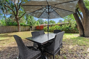 An outdoor patio with a table and chairs, surrounded by trees and a wooden fence.