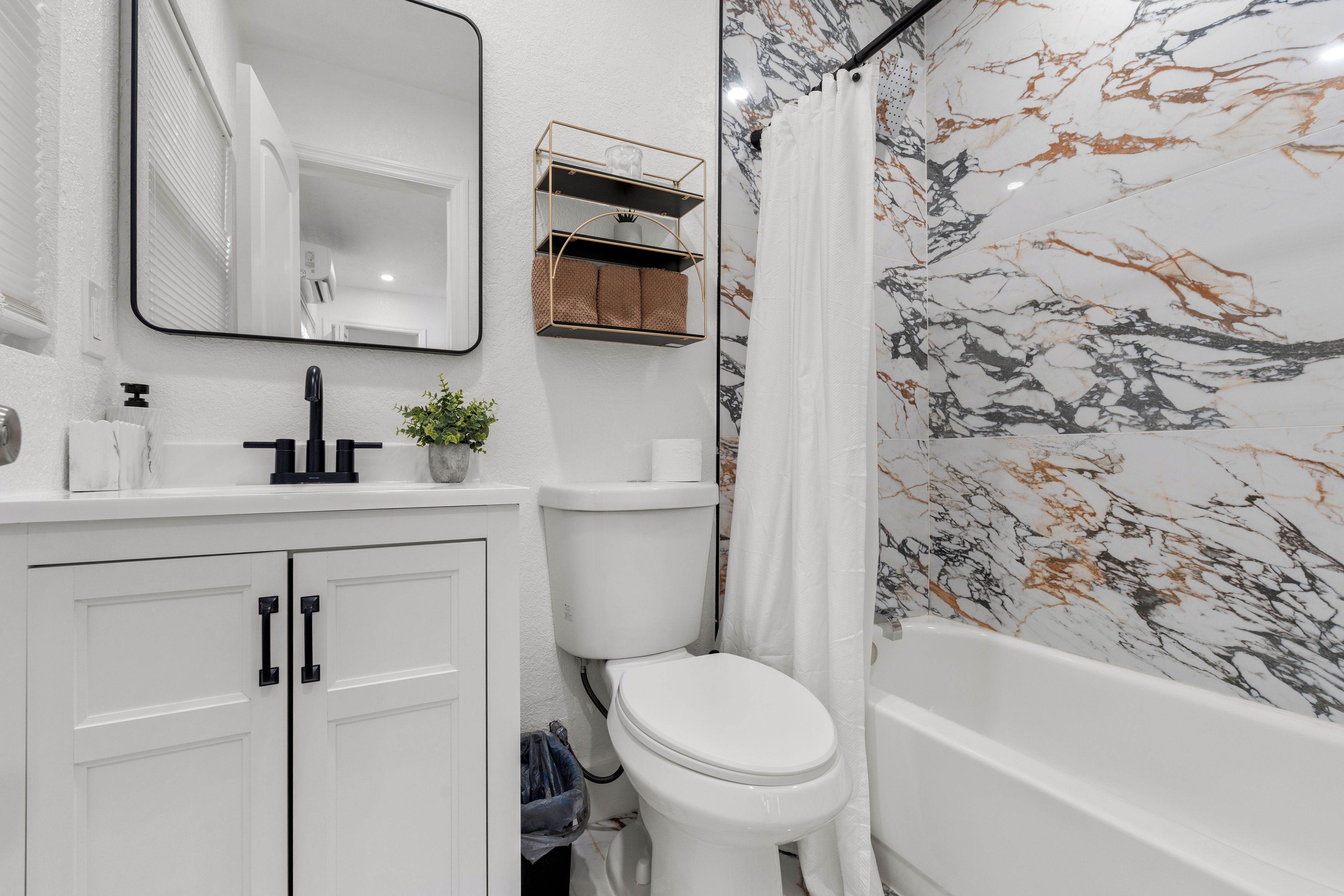 A bathroom with a white toilet, a sink with a mirror above it, a shower curtain, and a marble-patterned wall.