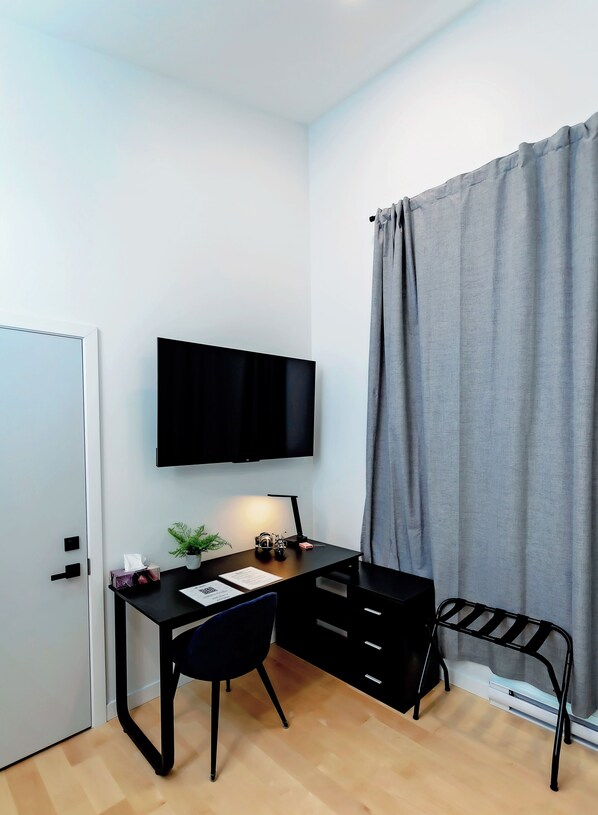 A compact room with a desk, chair, and a mounted TV. There's a door on the left and a curtain on the right.