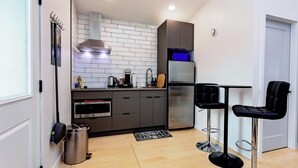 Une cuisine moderne équipée d’un four encastré, d’un réfrigérateur en acier inoxydable et d’une machine à café. On y trouve deux tabourets de bar noirs et une petite table.