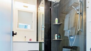 Une salle de bain moderne dotée d’une douche à parois de verre, de toilettes blanches et d’un meuble-lavabo avec un miroir et des rangements.