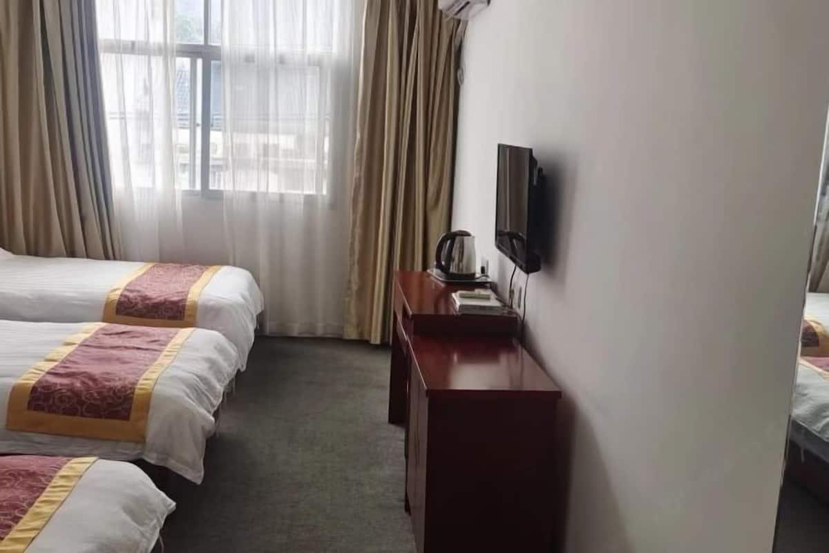 Habitación de hotel con dos camas, un escritorio con televisor y una ventana con cortinas.