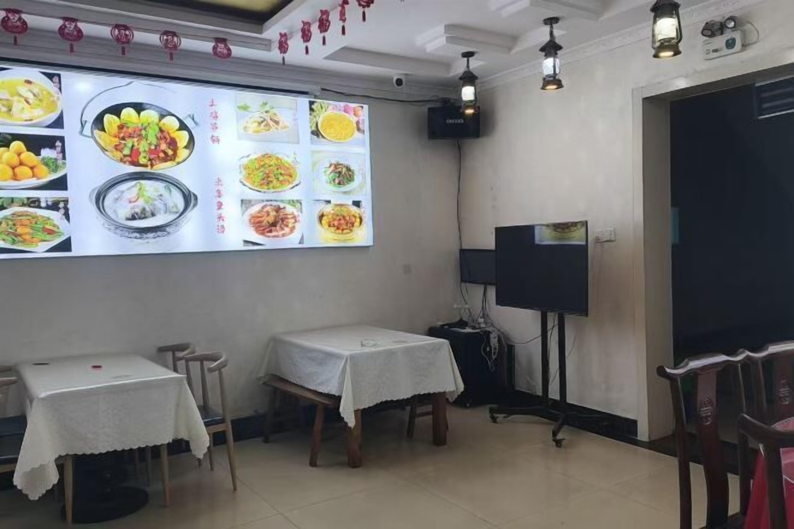 A dining area with tables and chairs, a wall-mounted menu display, and a projector screen.