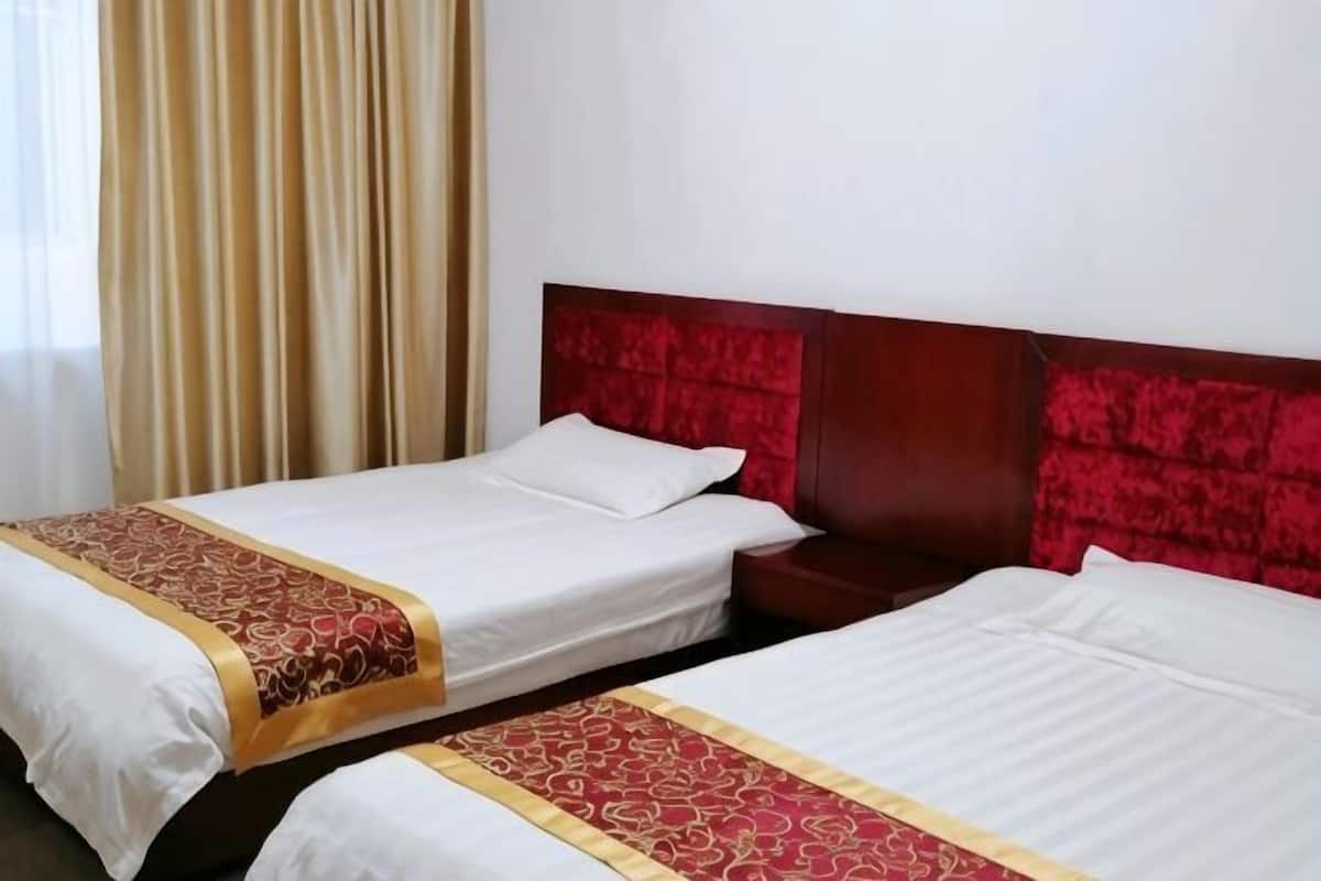 Dos camas individuales con cabeceros rojos, una mesita de noche de madera y una cortina color beige.