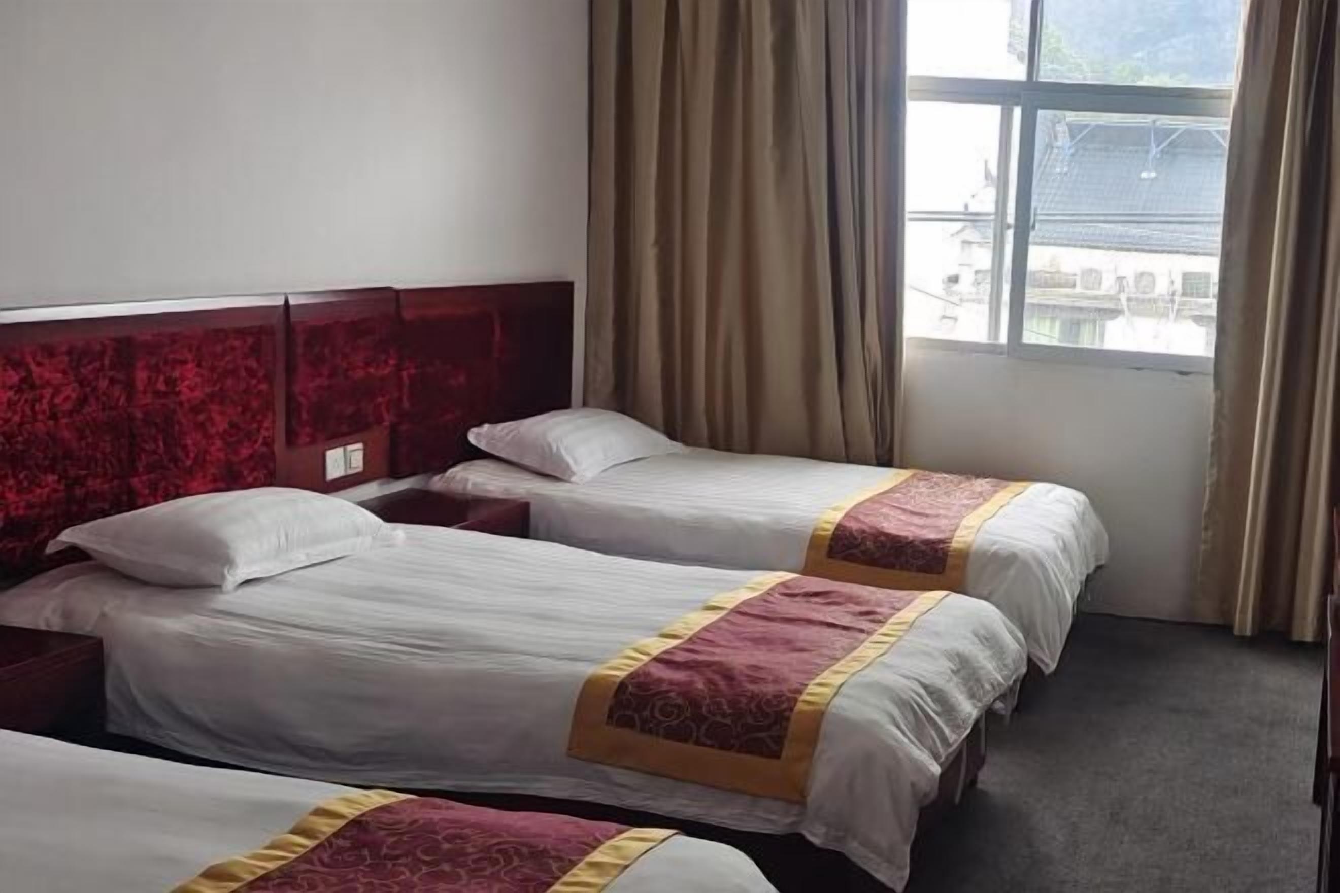 A hotel room with two beds, a wooden headboard, a window with curtains, and a view of buildings outside.