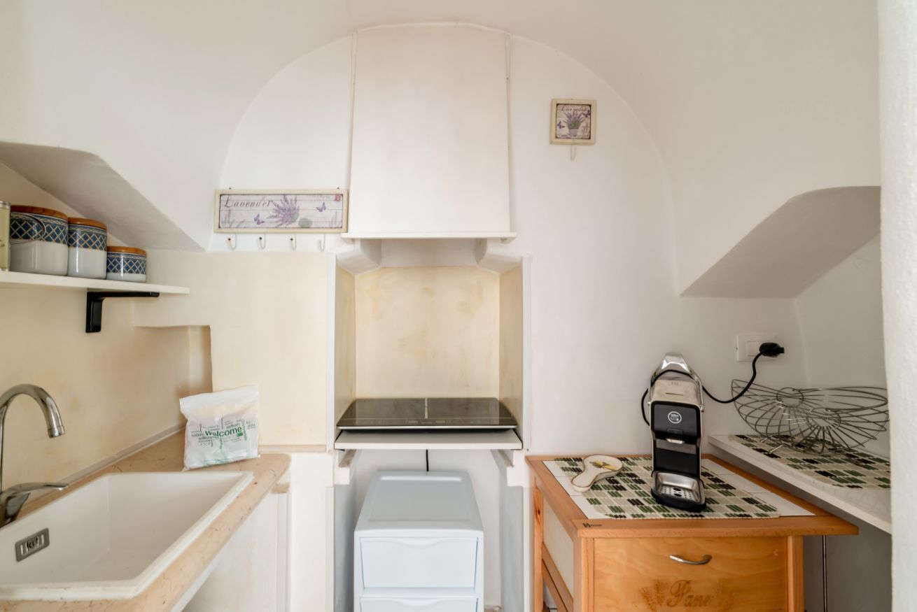 Een compacte keuken met een spoelbak, een kleine koelkast, een koffiezetapparaat en een kastje boven het fornuis.