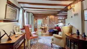 A cozy living room with wooden beams, a patterned rug, and a variety of seating options including a chair and a sofa.