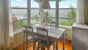 Un comedor con una mesa y sillas, un florero con flores y vistas a la vegetación y un cuerpo de agua a través de amplias ventanas.