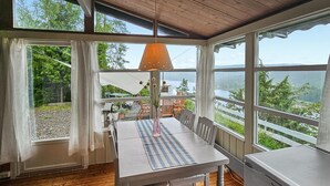 Comedor con una mesa lista para dos personas, una lámpara colgante y vistas a un lago y bosque a través de amplios ventanales.
