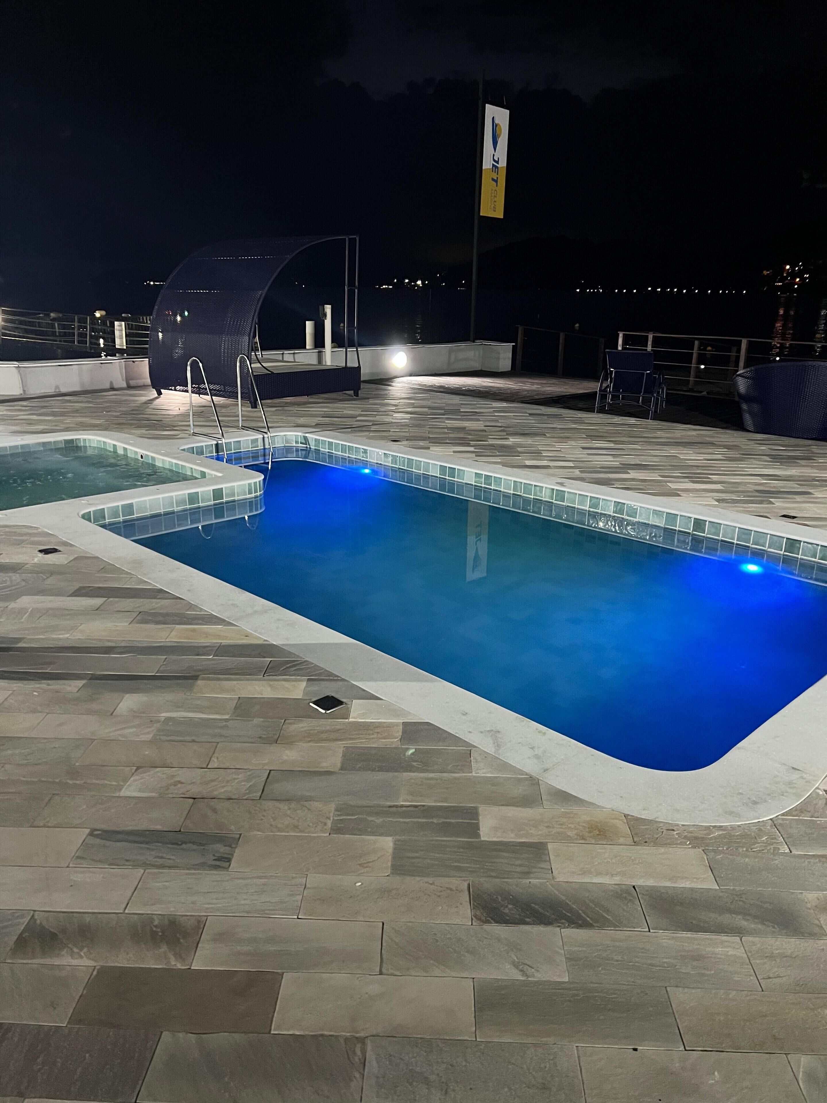 Ein Schwimmbecken mit einer gefliesten Kante und einer umlaufenden Stein-Terrasse.