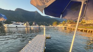 A wooden dock with a blue umbrella, a boat docked in the background, and a mountainous landscape. - Pousada Jet Club Marine Angra (Angra dos Reis)