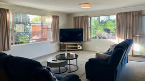 A living room with a flat-screen TV, two sofas, a coffee table, and large windows with curtains. - Home with spa, sauna, garden in prime location (Rotorua)