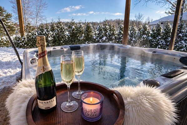 A hot tub with a bottle of Henkell Trocken and two glasses of wine on a tray, surrounded by a snowy landscape.