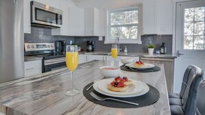 A modern kitchen with white cabinets, a marble countertop, and a dining area with a black chair.